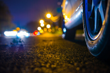 Night country road with glowing lanterns. Headlights of approaching cars. Close up view from the level of a parked car wheels.