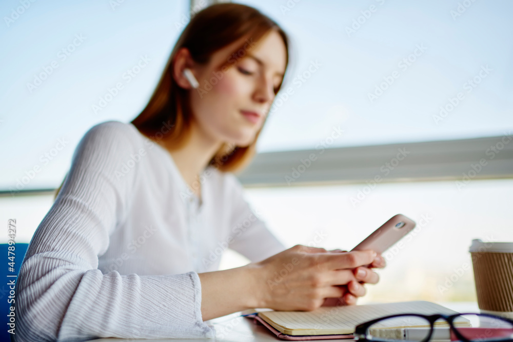 Poster side view of blurred female student sitting at table with education textbook and using mobile applic
