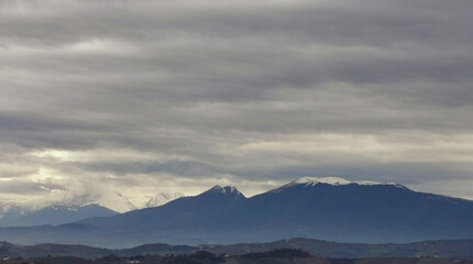 Fototapeta na wymiar Nuvole grigie sopra le montagne innevate