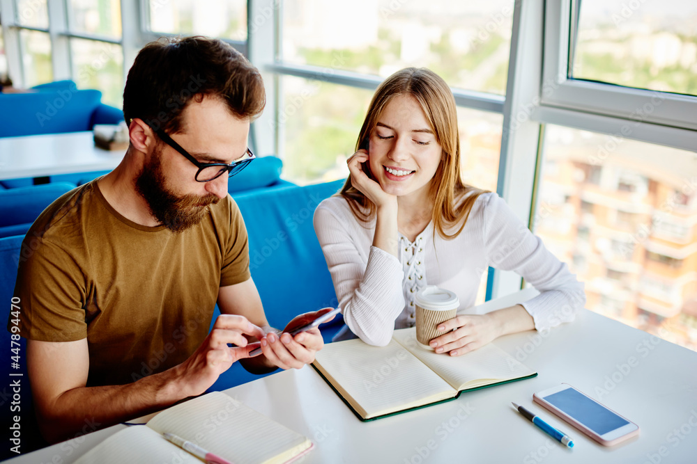 Aufkleber caucasian male blogger using cellphone device for network chatting while happy girlfriend with coffe