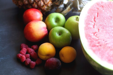 Watermelon, pineapple, apples, peaches, apricots, plum and raspberries on dark background. Selective focus.