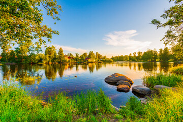 Houses on the banks of the river. Ducks swim in the pond. Sunset. Blue sky. Beautiful nature. Summer evening. View from the grassy shore.
