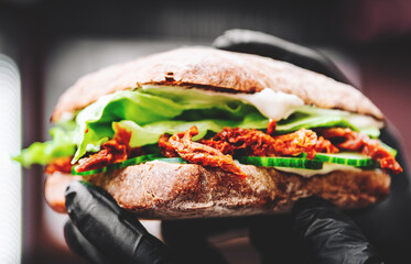 Vegetarian ciabatta sandwich with sun-dried tomato, cheese, cucumber and salad in hands