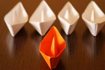 Several white paper boats and an orange one on the table.