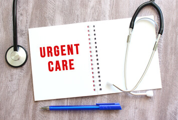 White notebook with red text URGENT CARE and a stethoscope on a gray wooden table.