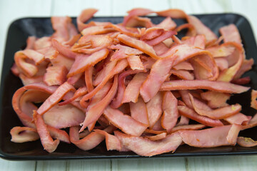 Squid (Lat. Teuthida) half-rings cut into strips on a black rectangular plate with a wooden table background. Food is a delicacy snack for beer.