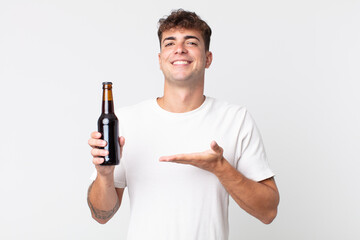 young handsome man smiling cheerfully, feeling happy and showing a concept and holding a beer bottle