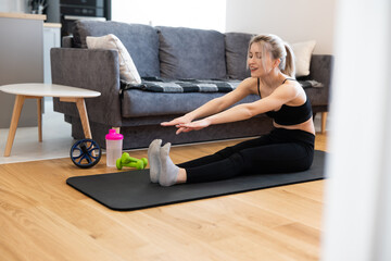 Sportswoman stretching on fitness mat at home