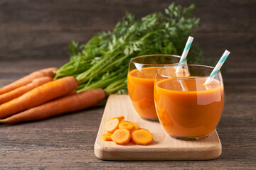 Fresh carrot smoothies and vegetables on a rustic wooden table, close-up.