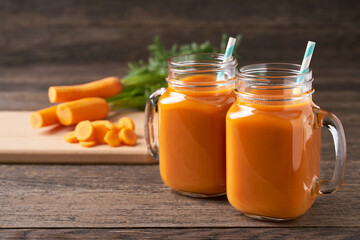 Fresh carrot juice in a mason jar glases and vegetables on a rustic wooden table.