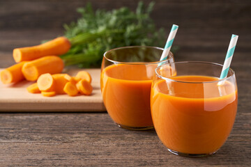 Fresh carrot smoothies and vegetables on a rustic wooden table, close-up.