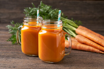 Fresh carrot juice in a mason jar glases and vegetables on a rustic wooden table.