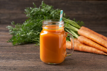 Fresh carrot juice in a mason jar glases and vegetables on a rustic wooden table.