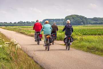 Two elderly unidentified couples with e-bikes cycle on a Dutch country road between fields in the...