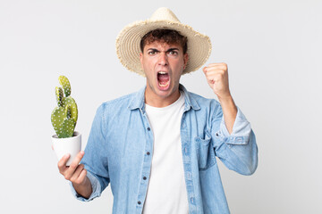 young handsome man shouting aggressively with an angry expression. farmer holding a decorative...