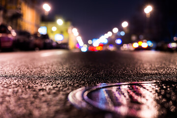 Rainy night in the big city, the headlights of the approaching cars on the road. Close up view of a hatch at the level of the asphalt