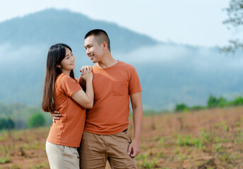 Portrait An Asian couple in identical brown shirts cuddling happily against a foggy and mountain backdrop.
