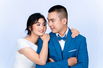 Pre-wedding portrait of a young Asian couple wearing bridal and groom outfits for a pre-wedding photoshoot together showing their love in a white background.