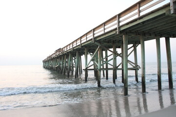 Beach scene with wooden pier over ocean at sunrise