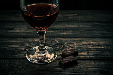 Glass of red wine with chocolate on an old wooden table. Close up view