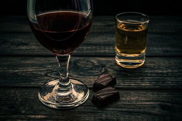 Glass of red wine and tequila with chocolate on an old wooden table. Close up view