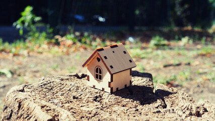 One toy wooden house stands on a wooden stand surrounded by a green blurry background, illustrates a mortgage, own housing, real estate rental