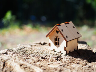 One toy wooden house stands on a wooden stand surrounded by a green blurry background, illustrates a mortgage, own housing, real estate rental