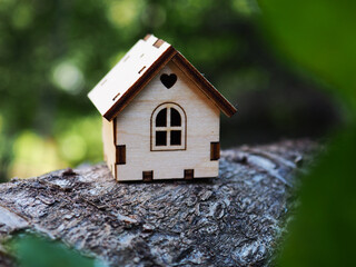One toy wooden house stands on a wooden stand surrounded by a green blurry background, illustrates a mortgage, own housing, real estate rental