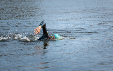Professional triathlete swimming in river's open water. Man wearing swim equipment practicing...