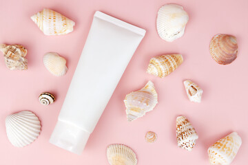 Unbranded white squeeze bottle cosmetic tube and a lot of different sea shells on pink background. Natural organic cosmetics. Cosmetics with sea salt and calcium. Summer flatlay, mockup.