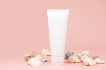 Unbranded white squeeze bottle cream tube and seashells a lot on pink background. Cosmetics with calcium and sea salt. Mockup, template, closeup, front view.