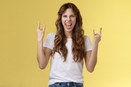 Going wild. Daring amused good-looking european curly-haired girl acting thrilled excited having fun enjoy awesome concert show yeah rock-n-roll heavy metal gesture grimacing satisfied