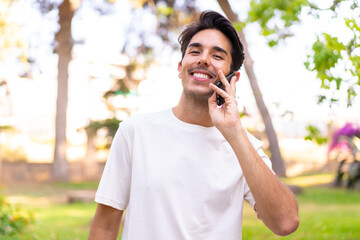 Young caucasian man in a park keeping a conversation with the mobile phone with someone