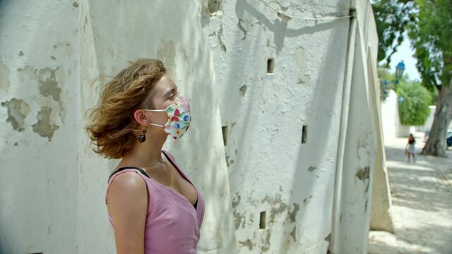 a woman in a protective mask in profile, a girl spends her vacation enjoying the architecture of an ancient city, against the background of an old, textured wall. The coronavirus is not a barrier to