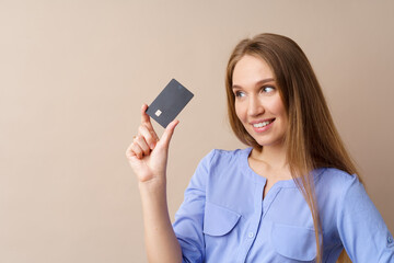 Naklejka premium Beautiful young woman holding black credit card against beige background