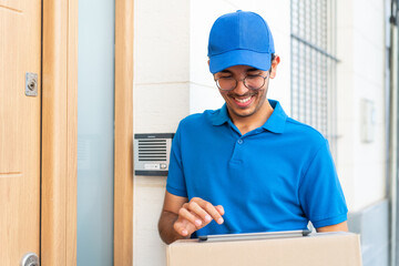 Young delivery man at outdoors signing on tablet and holding boxes