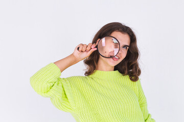 Young beautiful woman with freckles light makeup in sweater on white background with magnifier playful