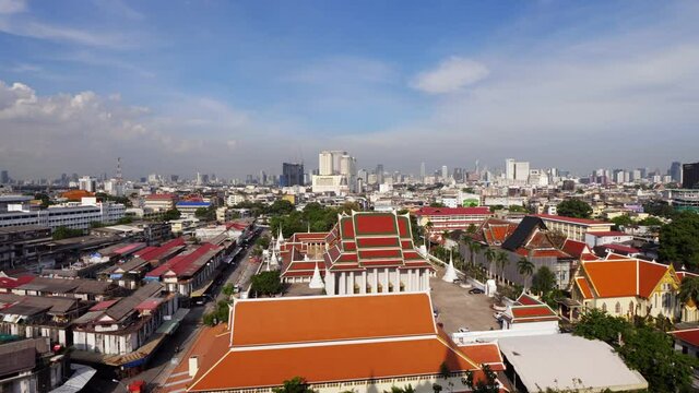 Move near silhouetted woman and look to Bangkok city, bright colored roofs of Buddhist temple buildings seen down. Modern towers seen at distance, scenic panorama of city from height