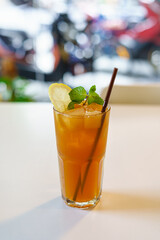 A Glass of Iced tea lemon with brown straw put on the white table.