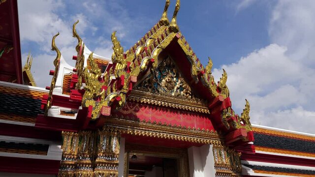 Mosaic decoration sparkle in gold under sun light, close view on decorated gable roof of building at Buddhist temple. Camera move around and looking up to shining ornamented facade