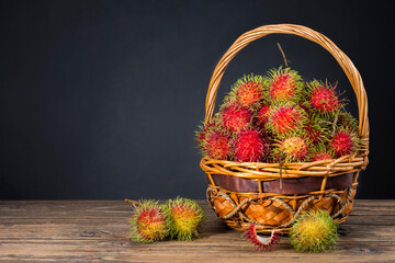 Fototapeta na wymiar Fresh sweet red rambutan Put in a basket on an old wooden table with a dark background, with space for copying text.