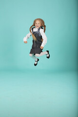 a beautiful little smiling blonde girl in a white shirt and a gray sundress a schoolgirl jumps
