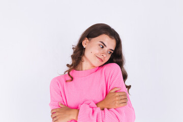 Young beautiful woman with freckles light makeup in sweater on white background hugging herself,...