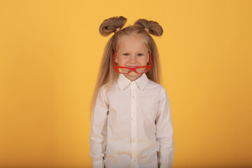 a beautiful little smiling blonde girl with red-rimmed glasses in a white shirt and a plaid skirt is a schoolgirl on a yellow background