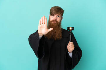 Redhead caucasian judge man isolated on blue background making stop gesture