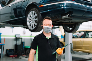 mechanic wearing surgical mask holding a clipboard working in garage. Repair service.