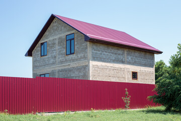 Private house under construction with windows and a roof behind a fence. Country housing.