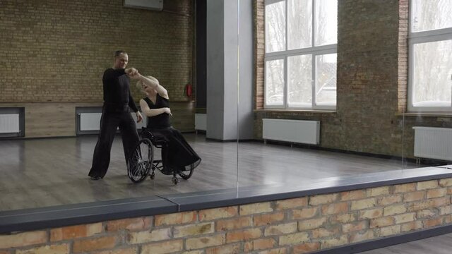 Professional ballroom dancers, middle aged man and woman with disability dancing in front of mirror. Disabled female on wheel chair and her dance partner preparing for competitions in ballroom