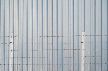 Barbed wire fence with the metal sheet wall in the background.