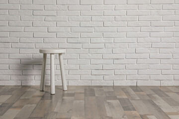 Stylish stool near white brick wall indoors. Space for text